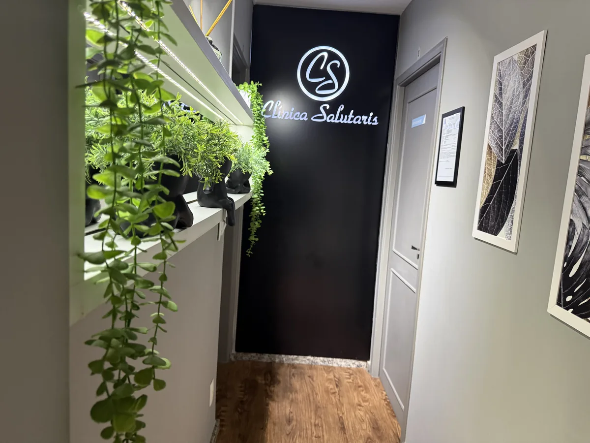 Corredor com plantas na prateleira e a parede preta com o logo iluminado